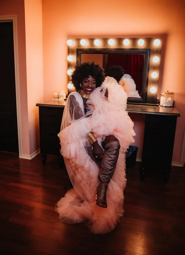 Elle, founder of Styled Nextdoor, smiling in a blush tulle gown at a lit vanity mirror